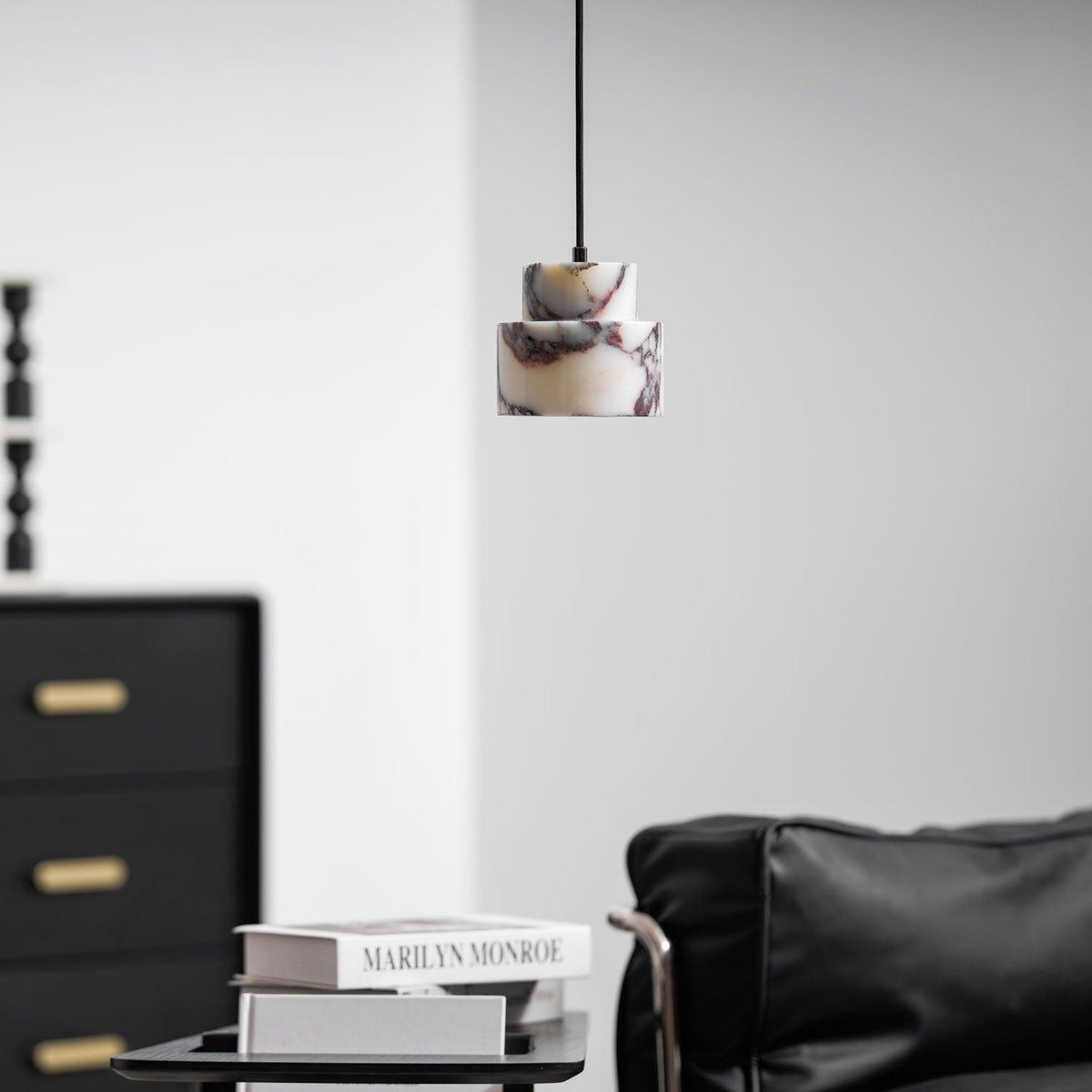 A small marble Clérachic pendant hangs high in a bright room, above a stack of books and a black leather armchair.