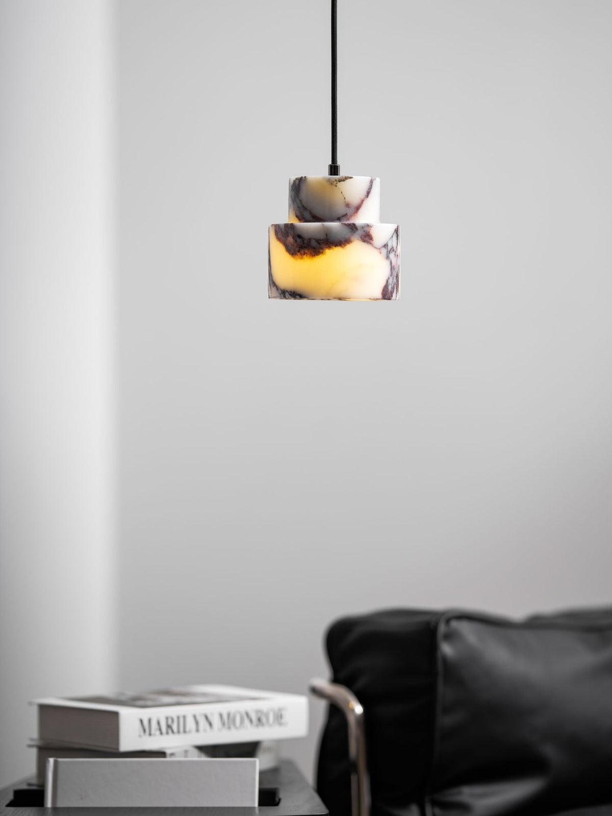 A small marble Clérachic pendant hangs in a pale room, with a leather chair and books on a low table beneath it.