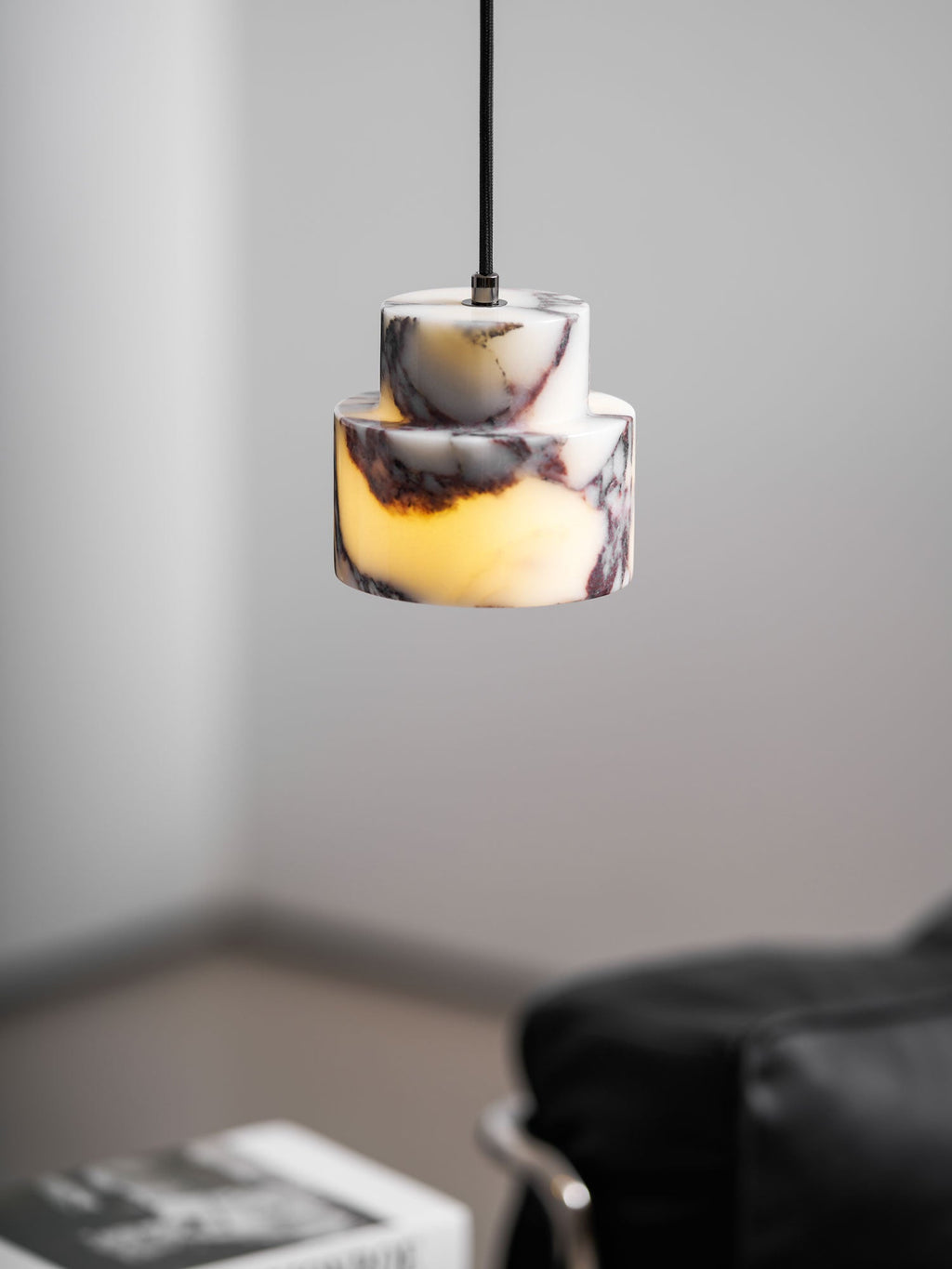 A lit marble Clérachic pendant seen at close range, with a leather seat and a stack of books softly blurred below.
