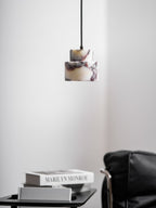 An unlit marble Clérachic pendant with plum veining hangs in a quiet corner, above a table of books and a leather chair.