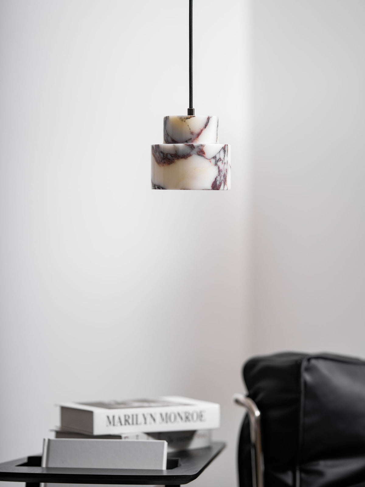 An unlit marble Clérachic pendant with plum veining hangs in a quiet corner, above a table of books and a leather chair.