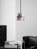 A marble Clérachic pendant hangs in a pale room, with a black cabinet and a leather armchair in the lower corner.