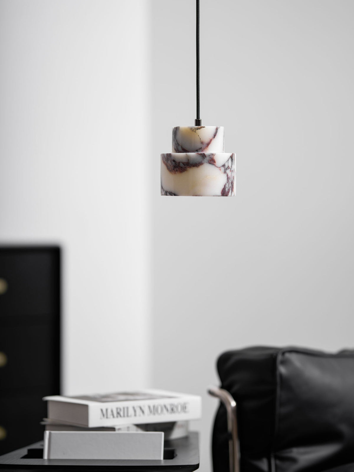 A marble Clérachic pendant hangs in a pale room, with a black cabinet and a leather armchair in the lower corner.