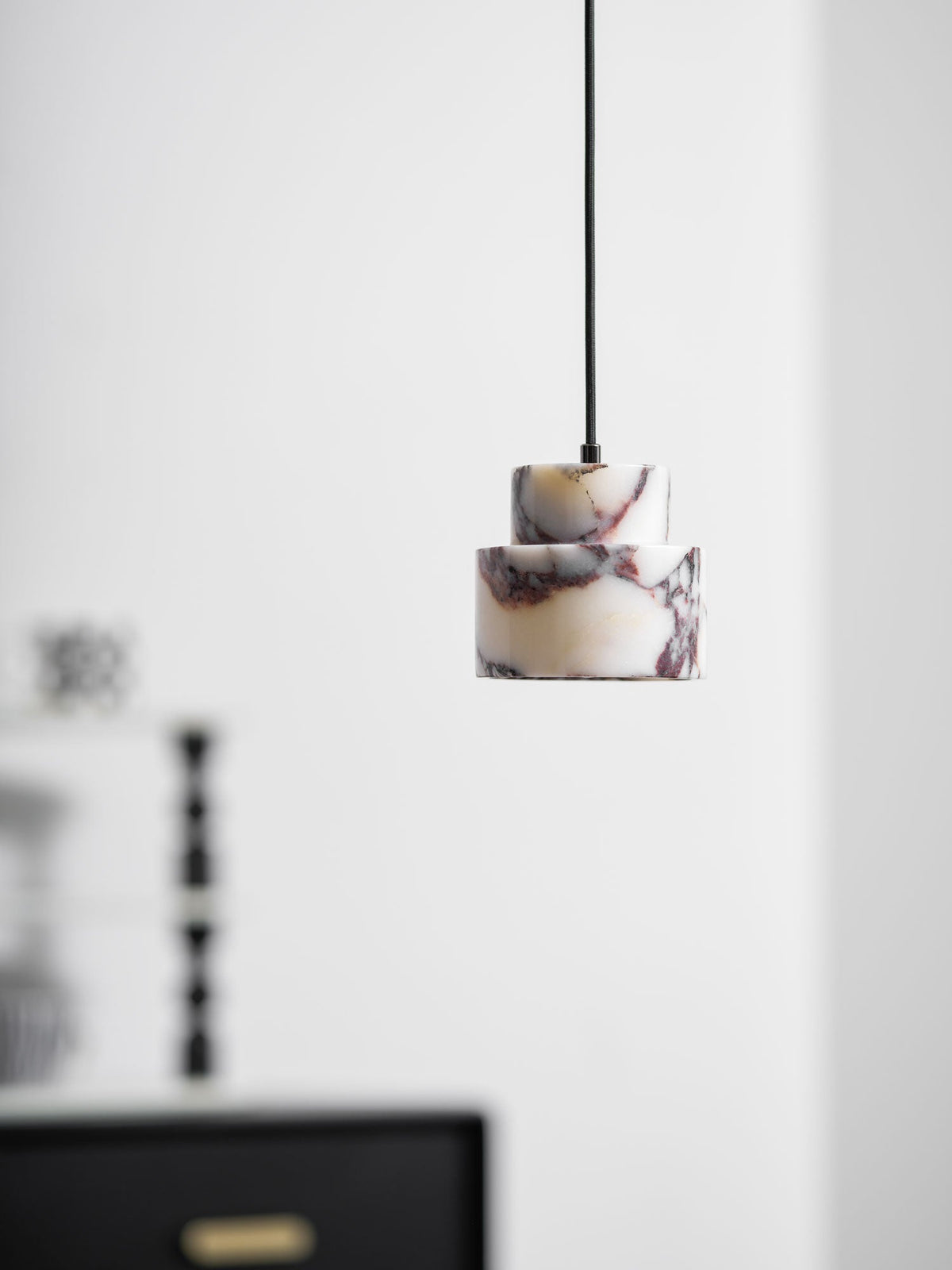 An unlit marble Clérachic pendant hangs off to the right, with a black chest and a shelf of black candlesticks to the left.