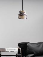 A small, unlit marble Clérachic pendant hangs against a pale wall, above a leather armchair and a book on a side table.