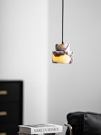 A lit marble Clérachic pendant hangs in a bright corner, with a black cabinet to the left and a stack of books below.