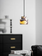 A marble Clérachic pendant glows amber at the centre, beside a black chest of drawers and a shelf of candlesticks.