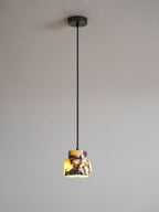 A small marble Clérachic pendant on a black cord and a dark ceiling cup, lit warm against a soft grey wall.