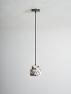 An unlit marble Clérachic pendant hangs from a dark ceiling cup on a long black cord, against a pale wall.
