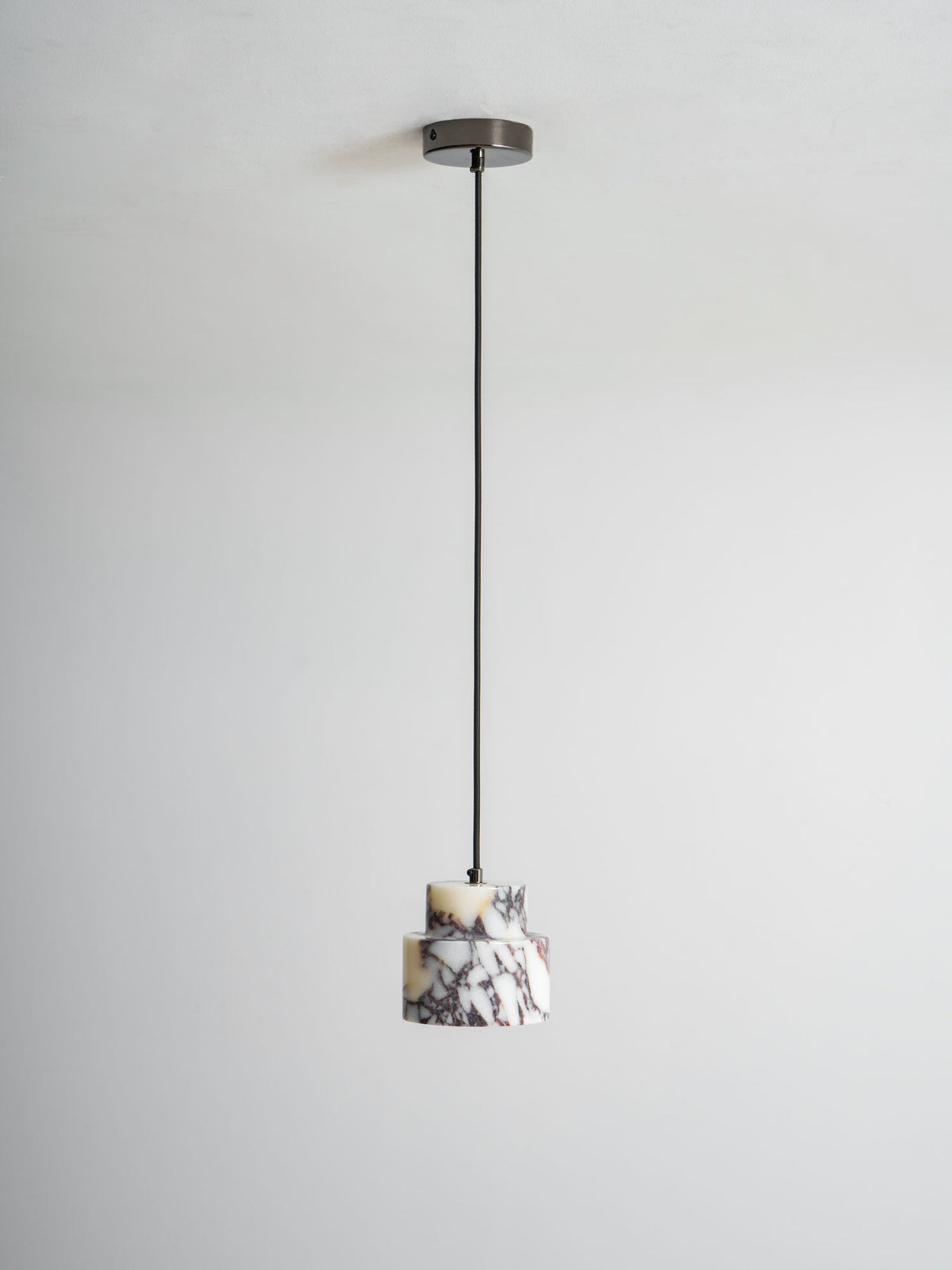 An unlit marble Clérachic pendant hangs from a dark ceiling cup on a long black cord, against a pale wall.