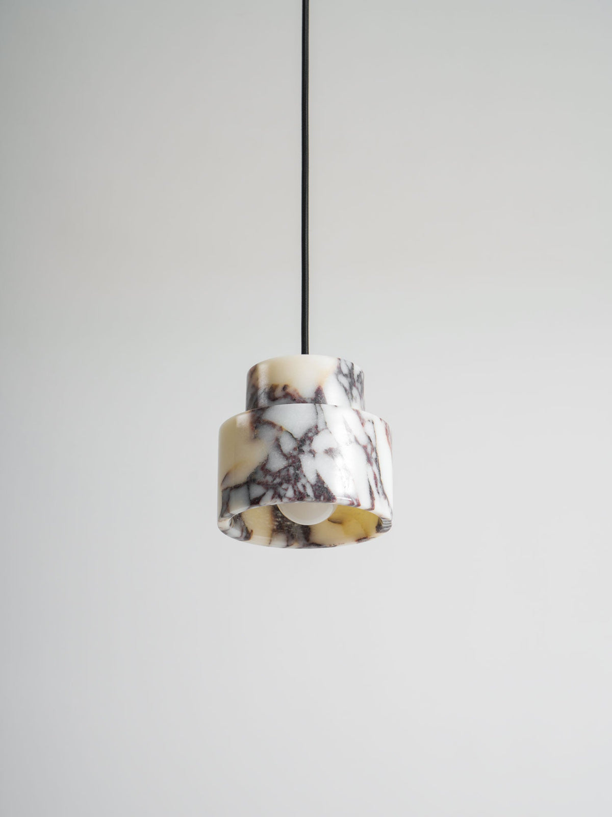 Underside view of the marble Clérachic pendant, with the bulb visible inside and a pale grey wall behind it.