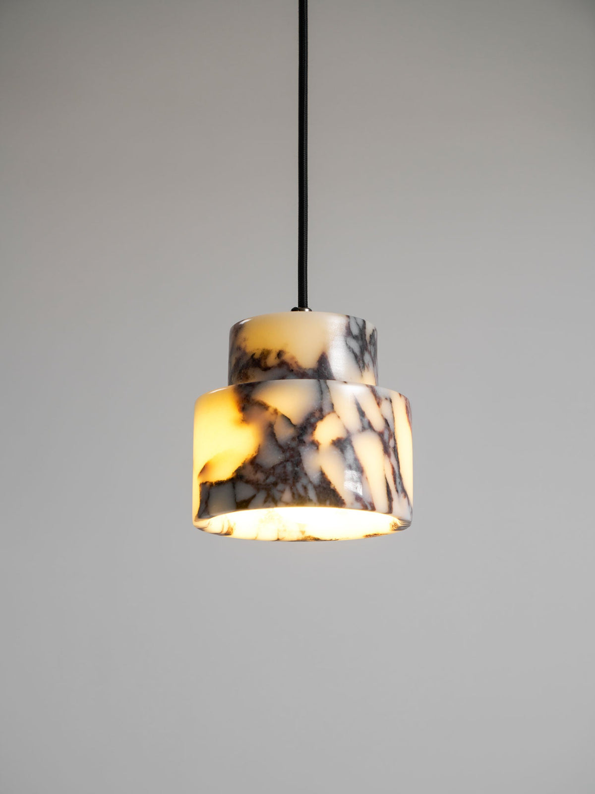 The stepped marble body of this Clérachic pendant glows warm amber, with dark veins, against a soft grey backdrop.