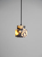A lit marble Clérachic pendant on a black cord, its purple-veined tiers glowing orange against a grey backdrop.