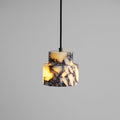 A close, lit view of the stepped marble Clérachic pendant on a grey backdrop, with amber light showing through the stone.
