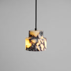 A close, lit view of the stepped marble Clérachic pendant on a grey backdrop, with amber light showing through the stone.