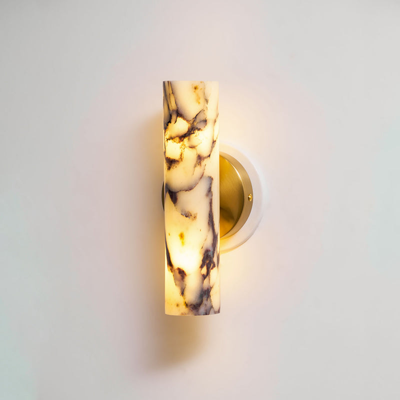 Close view of the lit marble shade and brass plate on this Clérachic wall light, the purple veining showing through the glow.