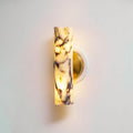 Close view of the lit marble shade and brass plate on this Clérachic wall light, the purple veining showing through the glow.