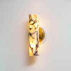 Close view of the lit marble shade and brass plate on this Clérachic wall light, the purple veining showing through the glow.