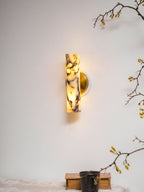 Small in the frame, this lit Clérachic wall light hangs above a shelf with a dark mug on a book, with blossom twigs at the edges.