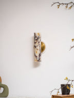 Unlit Clérachic wall light with a purple-veined marble shade, on a white wall above a green vase and a mug on a book.
