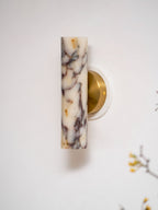 Close view of the unlit marble shade on this Clérachic wall light, the purple and gold veining clear against a white wall.