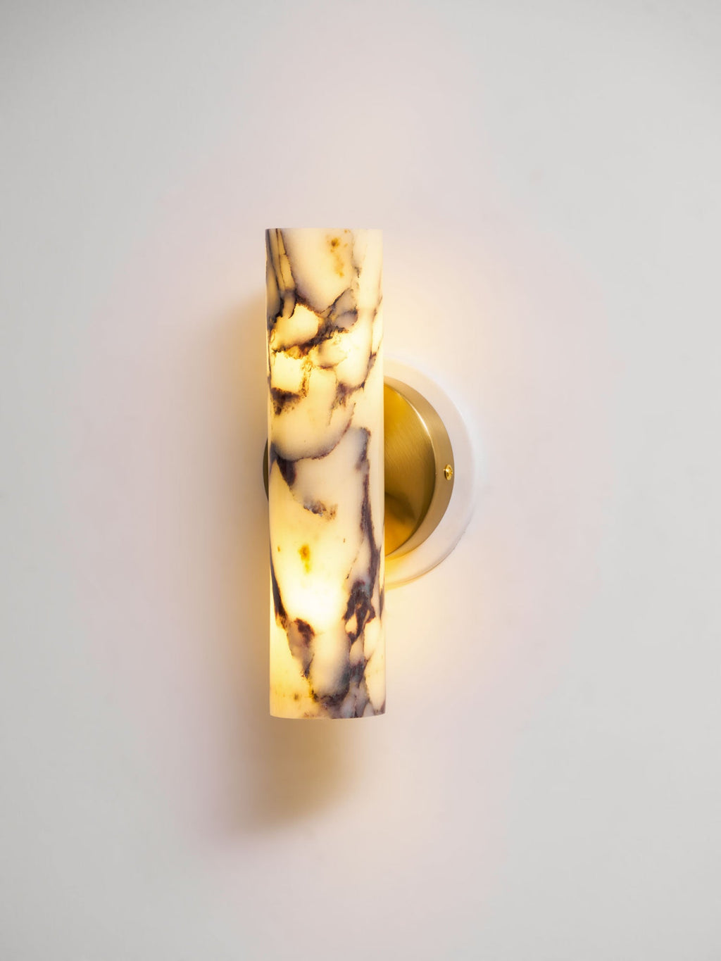 Lit Clérachic wall light on a pale wall, the marble shade glowing warm with dark purple veins and a brass back plate.
