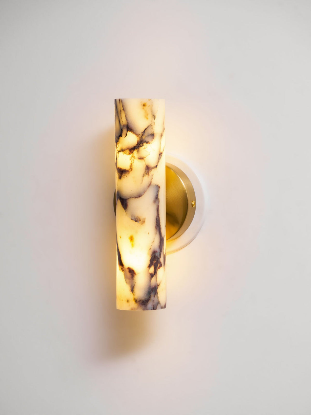 Lit Clérachic wall light on a pale wall, the marble shade glowing warm with dark purple veins and a brass back plate.