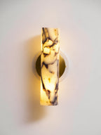 Close view of the lit marble shade of this Clérachic wall light, glowing gold at its base against a pale wall.