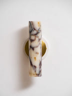 Front view of the unlit marble shade on this Clérachic wall light, sitting over a round brass plate on a white wall.