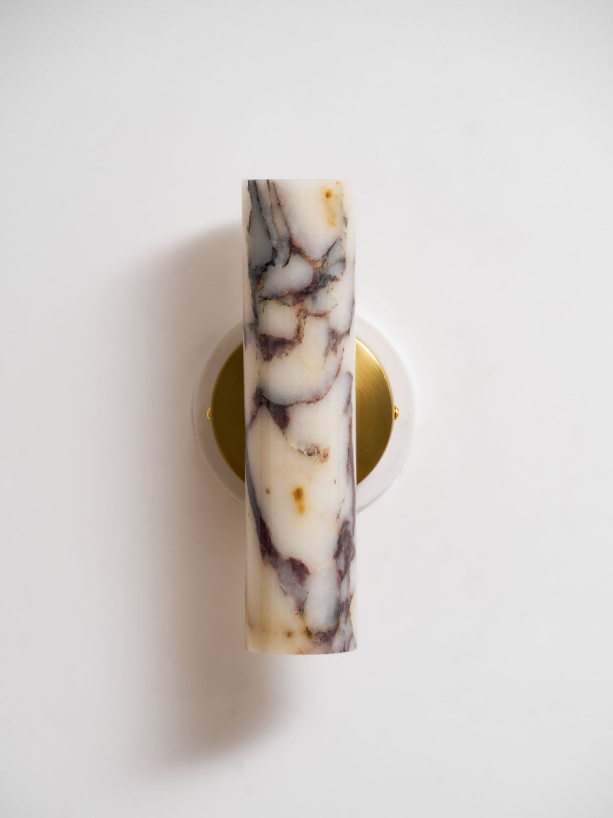 Front view of the unlit marble shade on this Clérachic wall light, sitting over a round brass plate on a white wall.