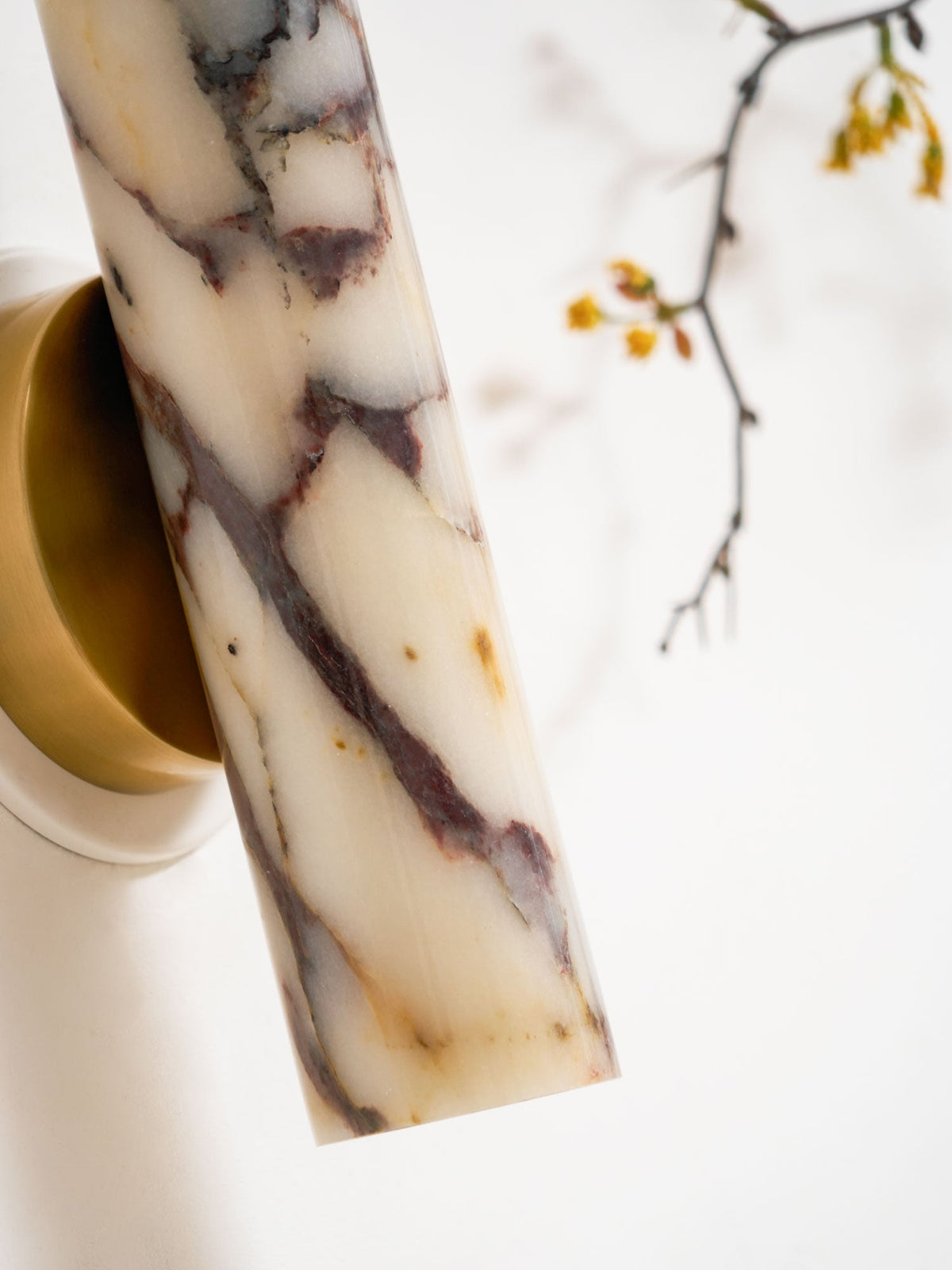 Close, angled view of the marble shade tilted out from the brass mount on this Clérachic wall light, with a blossom twig behind.