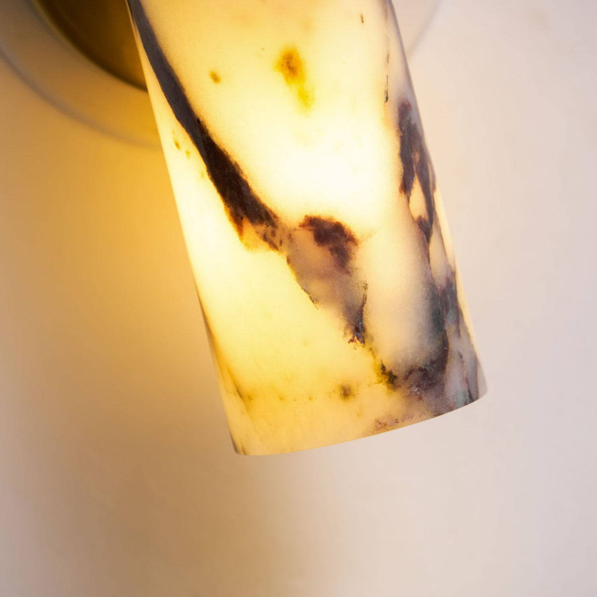 Underside view of the lit marble shade on this Clérachic wall light, light glowing through the stone near the open end.