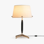 This Clérachic table lamp on a plain white backdrop, an off-white fabric shade on a dark wood stem and a three-legged brass base.