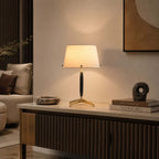 Lit Clérachic table lamp on a fluted wood sideboard, with a stone bowl, a sculptural ornament and a stack of books beside it.