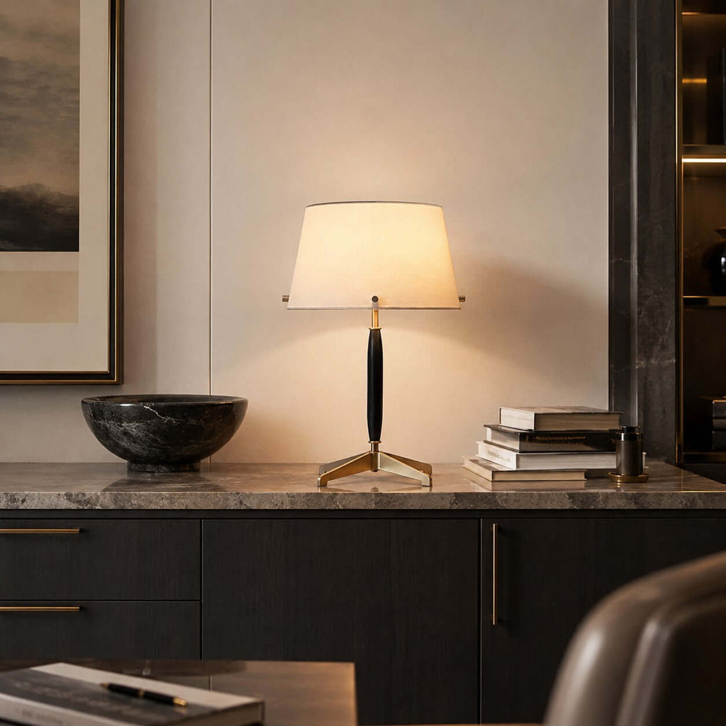 Warm light from this Clérachic table lamp on a marble-topped dark cabinet, next to a black stone bowl and a pile of books.