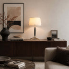 A Clérachic table lamp on a long walnut sideboard in a living room, under an abstract print, with a sofa and marble coffee table.