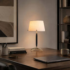 This Clérachic table lamp on a dark wood desk with a closed laptop, a pen pot and books, a framed print on the wall behind.