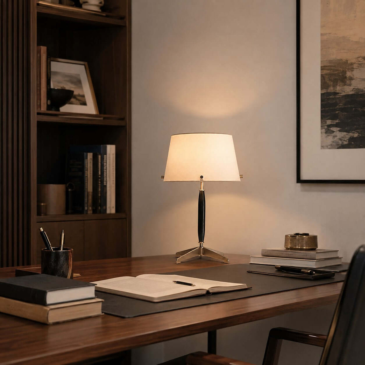 Clérachic table lamp on a dark desk in a study, with an open notebook, a pen pot and books, and a bookcase at the back.
