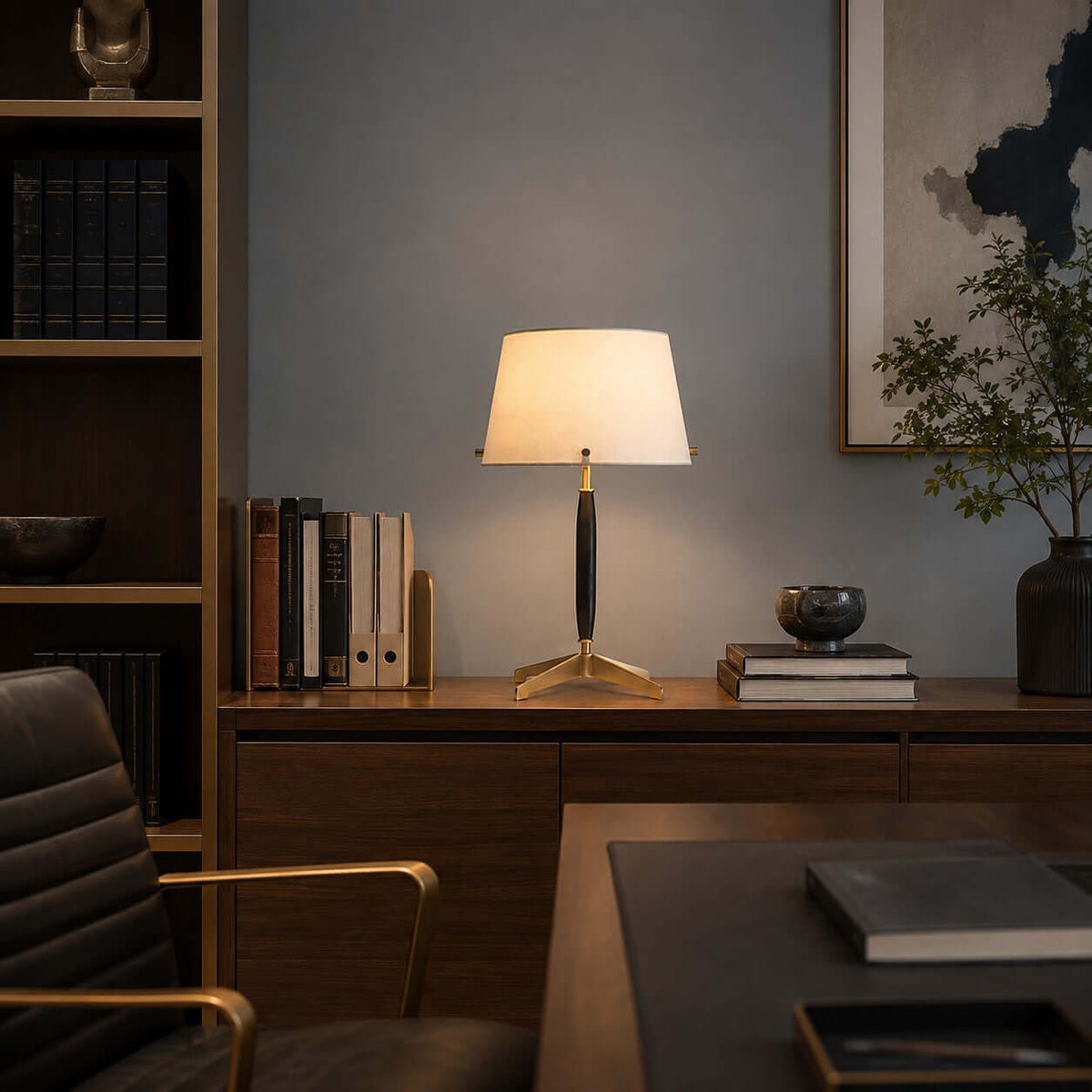 On a walnut credenza in a study, this Clérachic table lamp stands among books, a dark ceramic pot and a leafy stem in a vase.