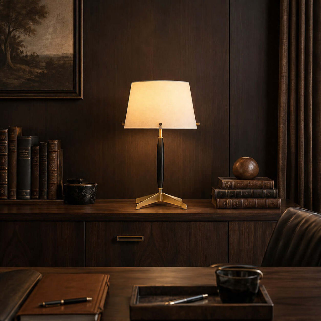 Lit Clérachic table lamp on a dark wood credenza with leather-bound books, a wooden sphere and a pen resting on a leather tray.