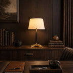 Lit Clérachic table lamp on a dark wood credenza with leather-bound books, a wooden sphere and a pen resting on a leather tray.