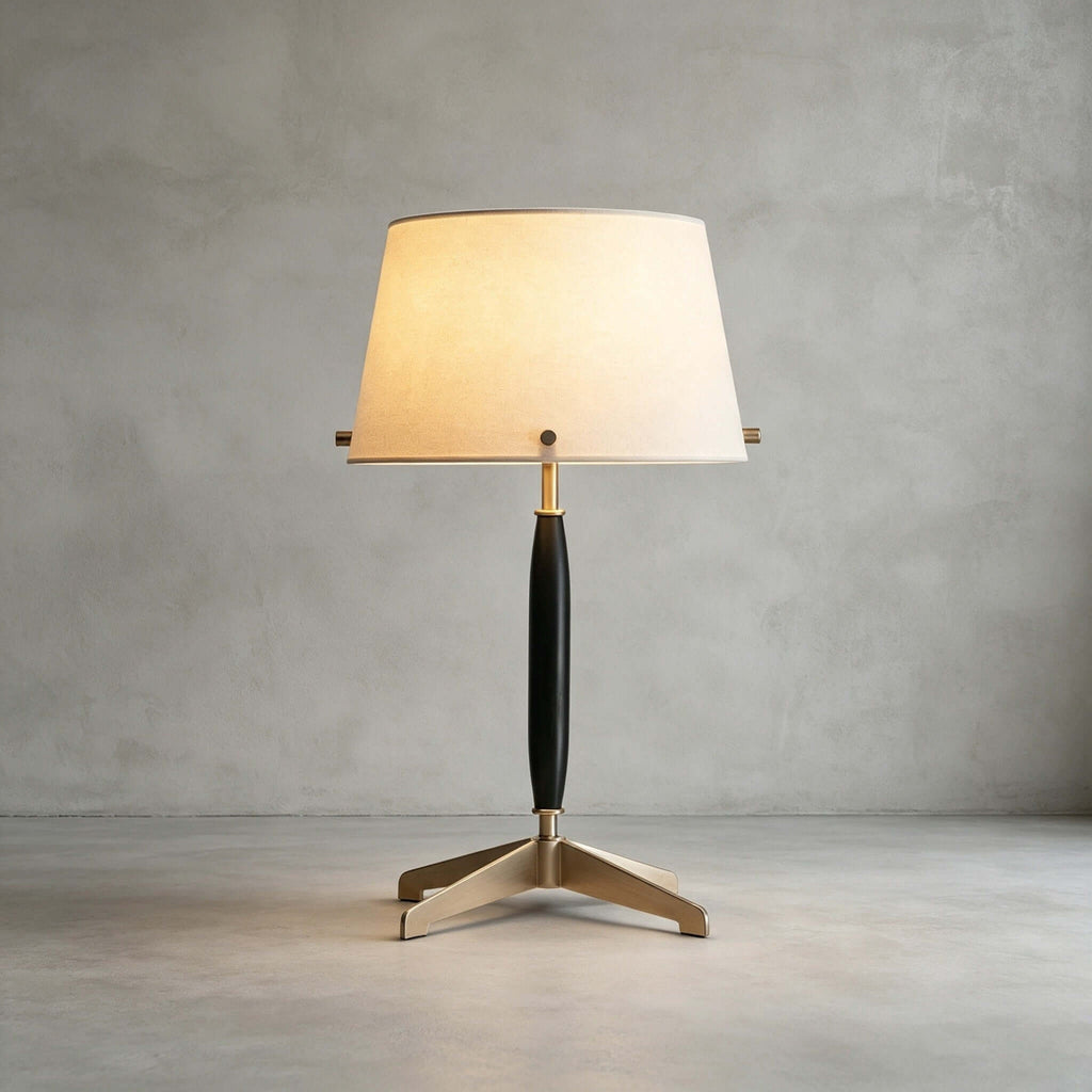 This Clérachic table lamp, unlit, stands on a polished concrete floor against a grey plaster wall, showing its dark stem and brass feet.