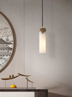 A lit Clérachic Quiver Pendant Light glowing warm above a marble-topped console, beside a round framed artwork and a small brass bird sculpture.