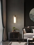 Clérachic Quiver Pendant Light glowing against a deep grey plaster wall, lighting a bonsai on the cabinet below in a quiet sitting room.