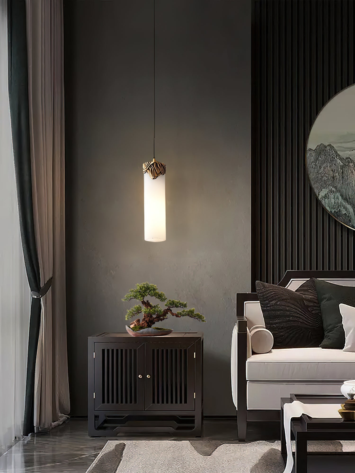 Clérachic Quiver Pendant Light glowing against a deep grey plaster wall, lighting a bonsai on the cabinet below in a quiet sitting room.