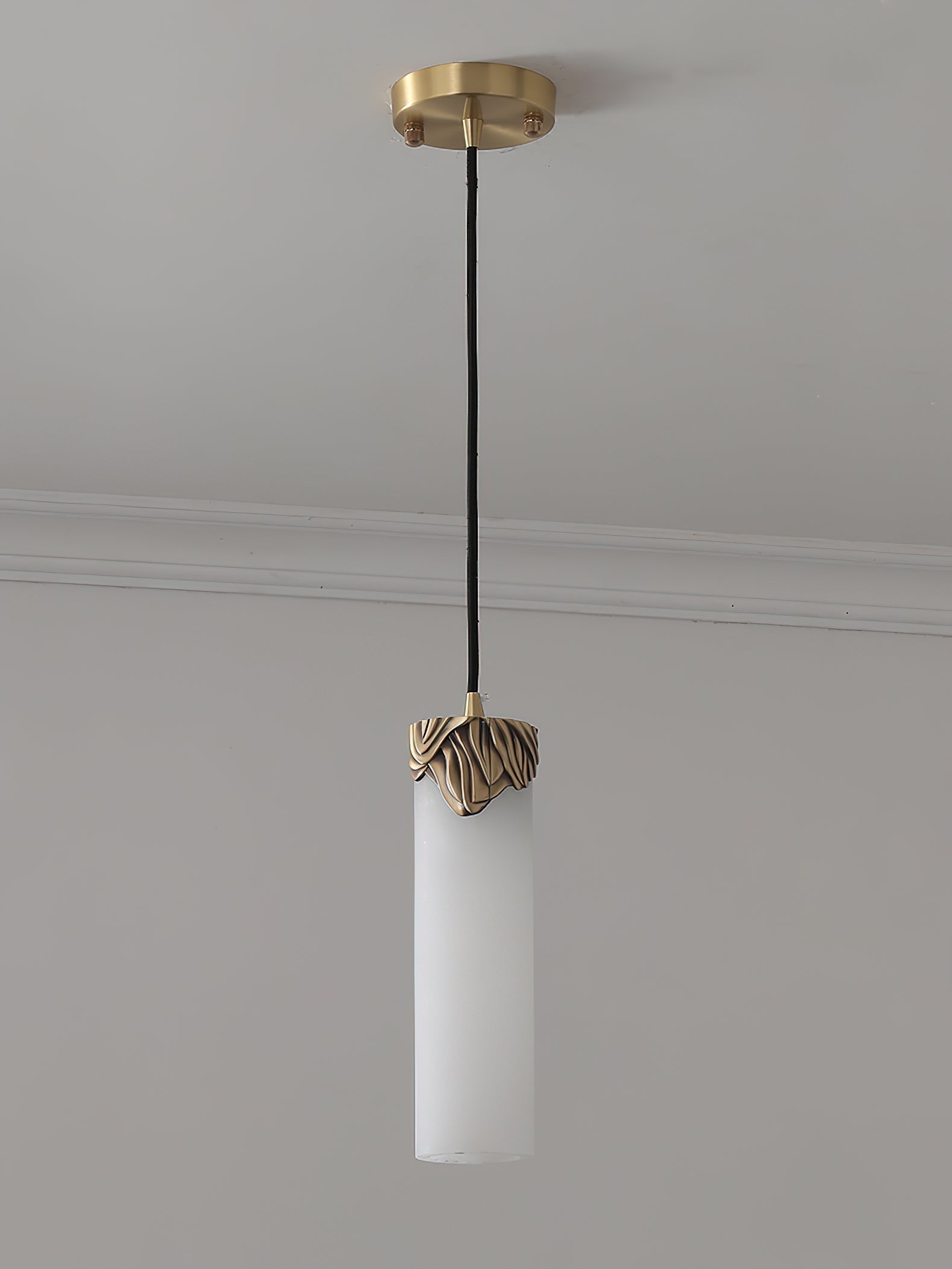 Unlit Clérachic Quiver Pendant Light installed on a plain ceiling, showing the pale matte stone, brass canopy and black fabric cord.