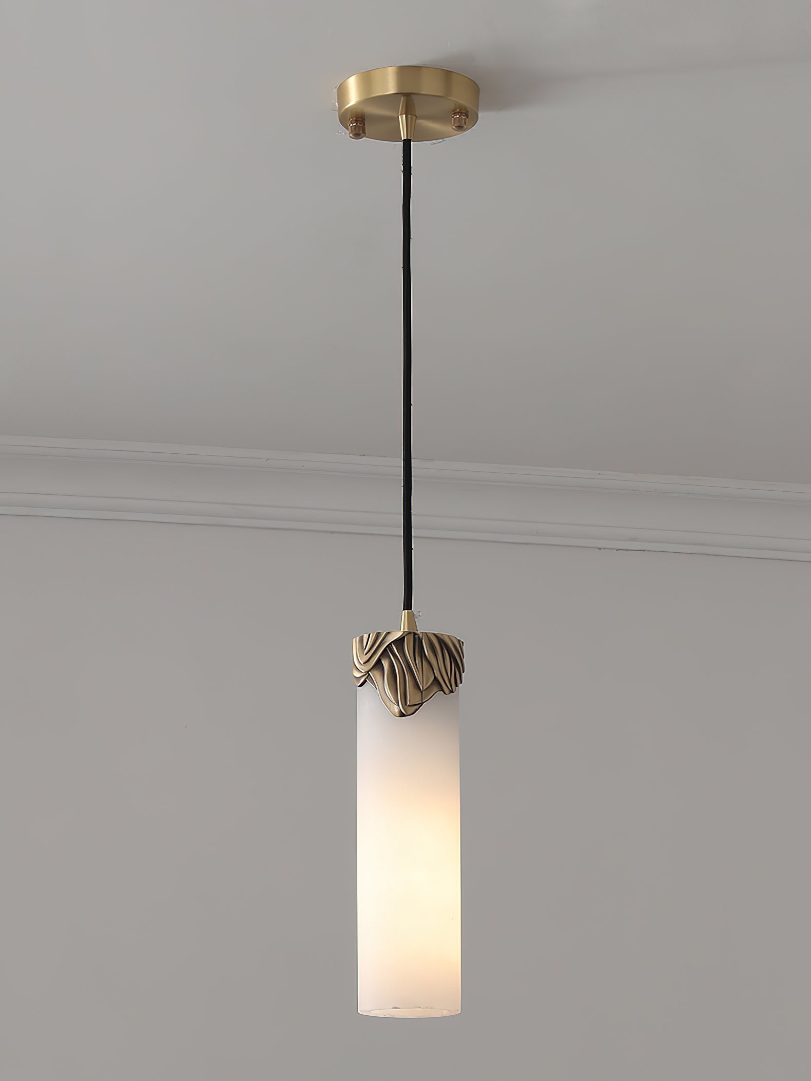 Clérachic Quiver Pendant Light switched on against a plain wall, warm light travelling through the stone instead of spilling from the bulb.