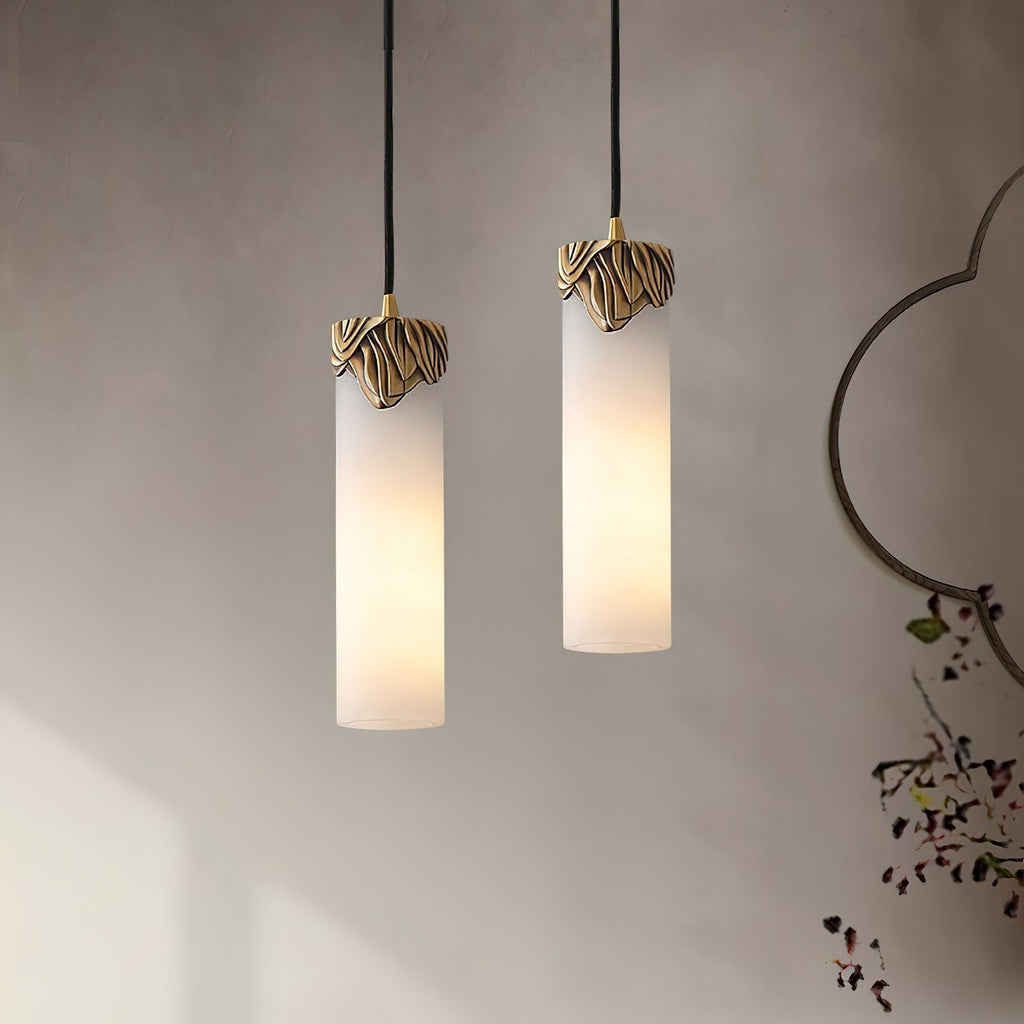 Both sizes of the Clérachic Quiver Pendant Light lit side by side on a limewash wall, the short and tall columns hung at different heights.