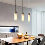 Row of three Clérachic Quiver Pendant Lights lit above a walnut dining table, spaced evenly over brass bowls in an open modern kitchen.