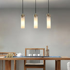 Three Clérachic Quiver Pendant Lights in a line above a wooden tea table, their warm columns lit over a teapot and small cups.
